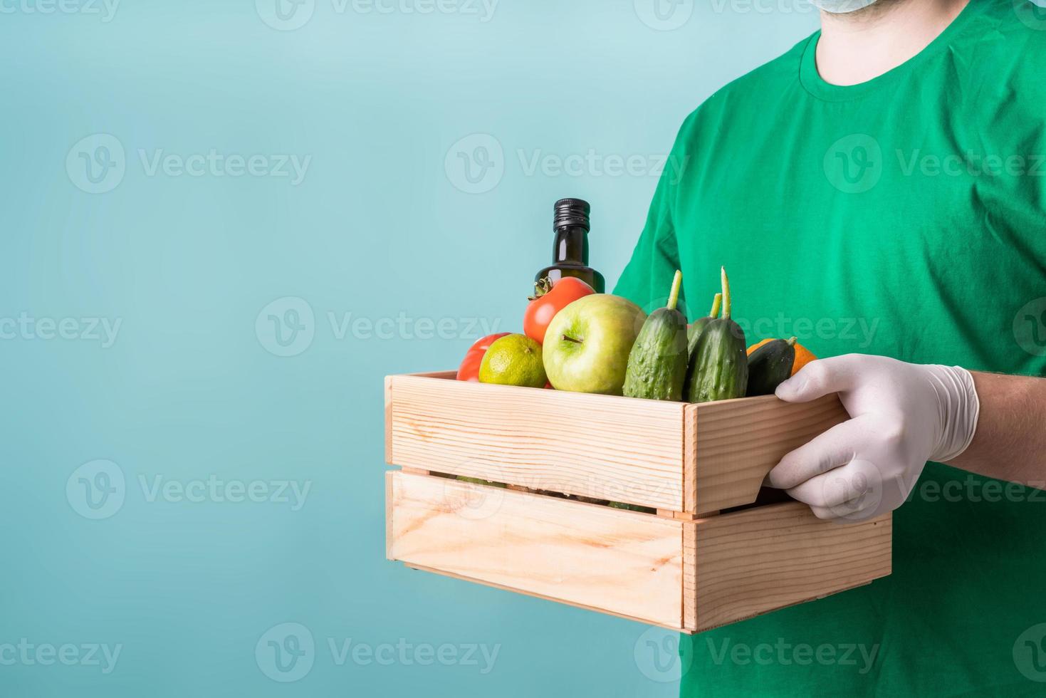 hombre en guantes sosteniendo una caja de madera llena de verduras foto