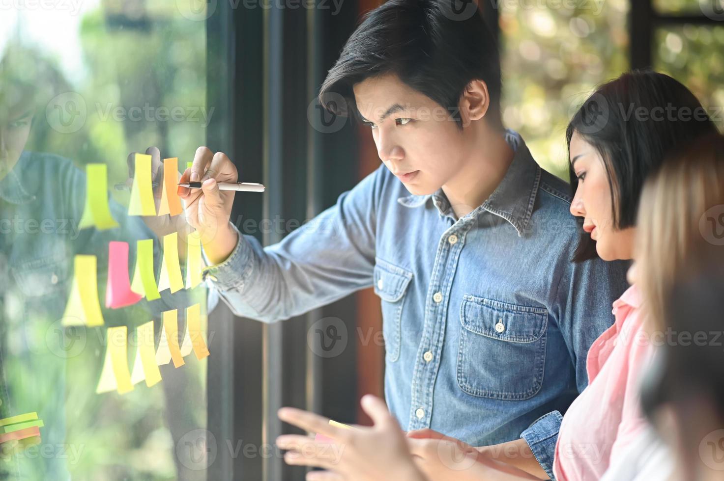 A group of young businessmen are planning for future projects. They outline the plan on the paper attached to the glass. photo