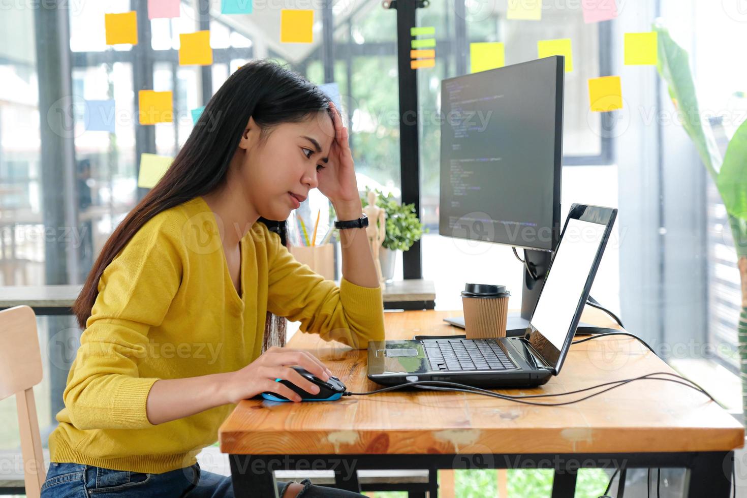 Asian female programmer wears a yellow shirt, looks at the laptop screen and shows a serious pose. photo