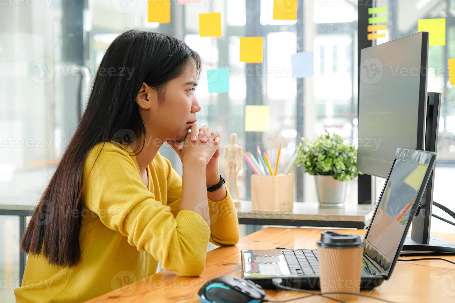 Asian female programmer for yellow shirt sitting with a hand on her chin,She stared at the computer screen and pondered. photo