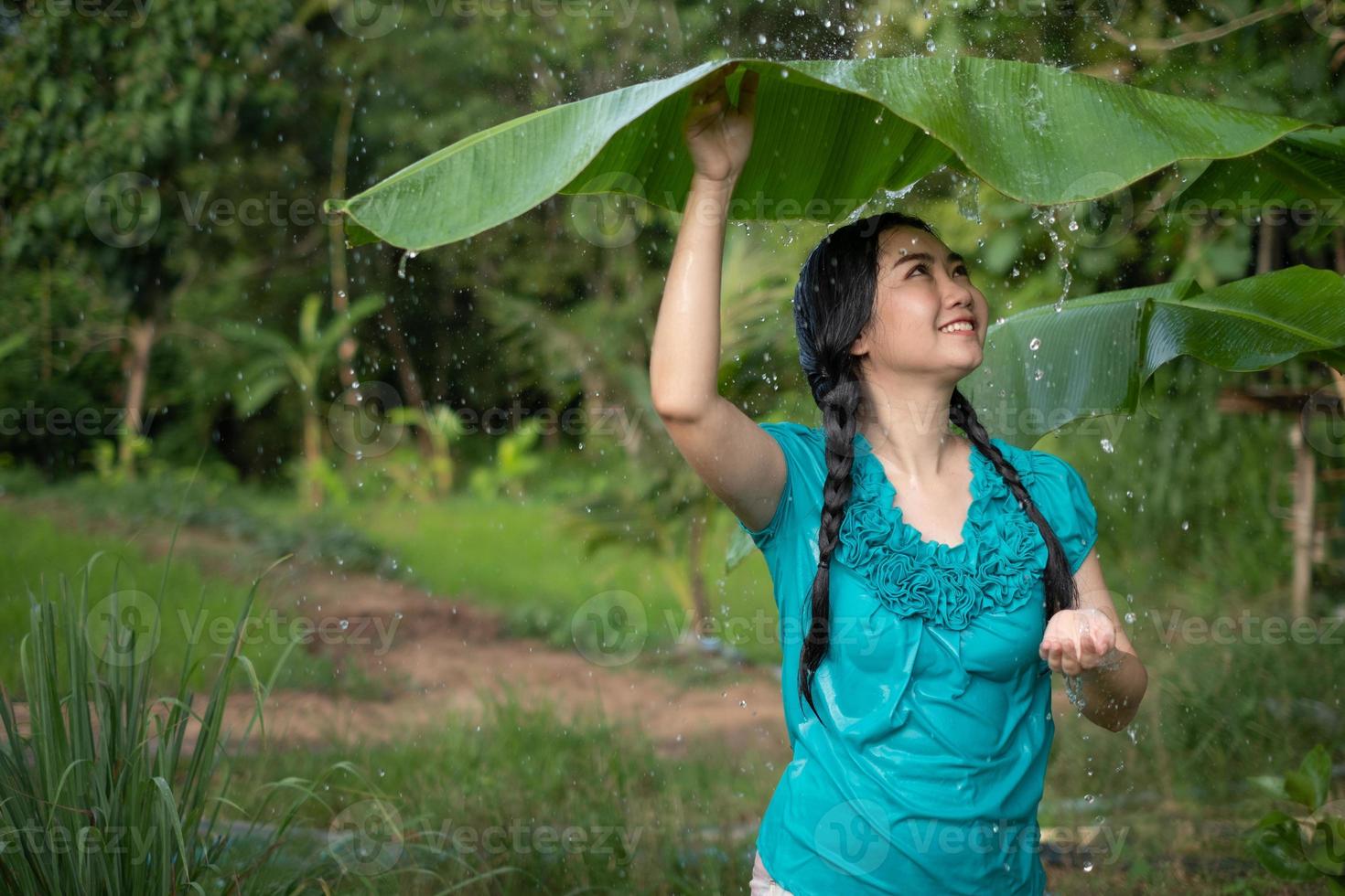 Retrato de una joven mujer asiática con cabello negro sosteniendo una hoja de plátano en la lluvia en el fondo del jardín verde foto