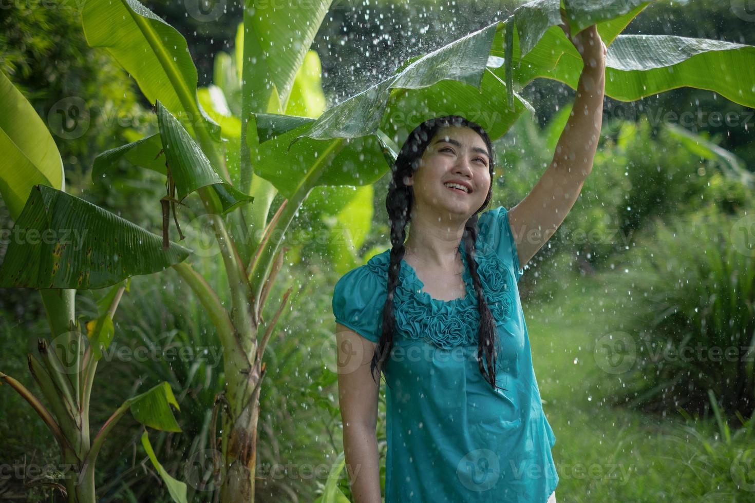 Portrait of a young Asia woman with black hair holding a banana leaf in the raining at the green garden background photo