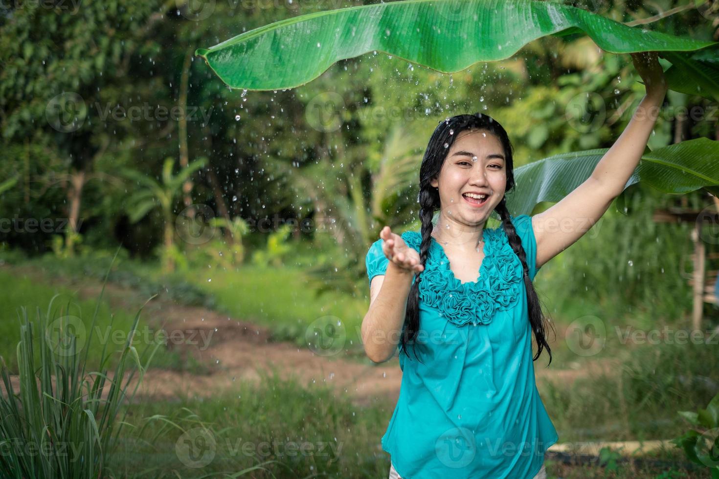 Retrato de una joven mujer asiática con cabello negro sosteniendo una hoja de plátano en la lluvia en el fondo del jardín verde foto