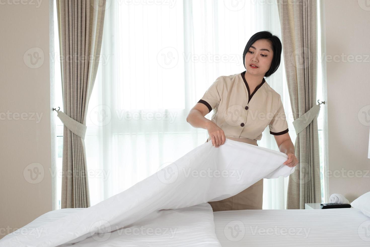 Young beautiful Asia maid arranging blanket on the bed in hotel room photo