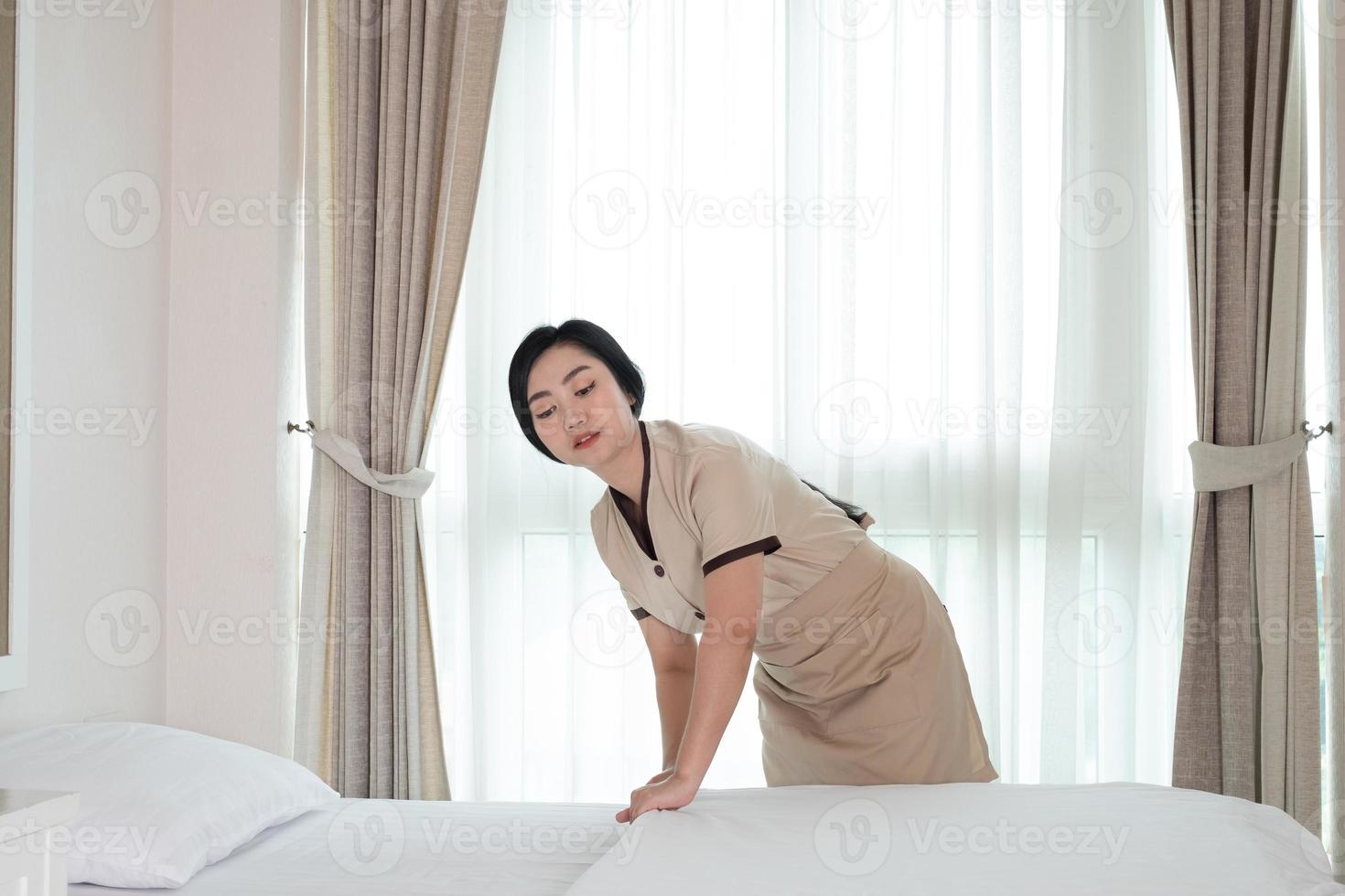 Joven y bella sirvienta de Asia arreglando una manta en la cama en la habitación del hotel foto