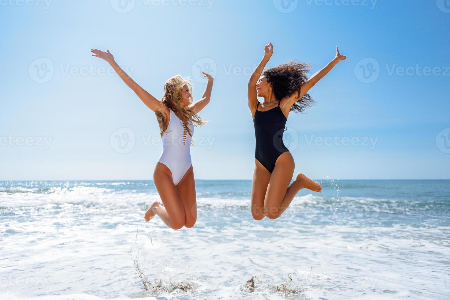 Dos chicas divertidas en traje de baño saltando en una playa tropical foto