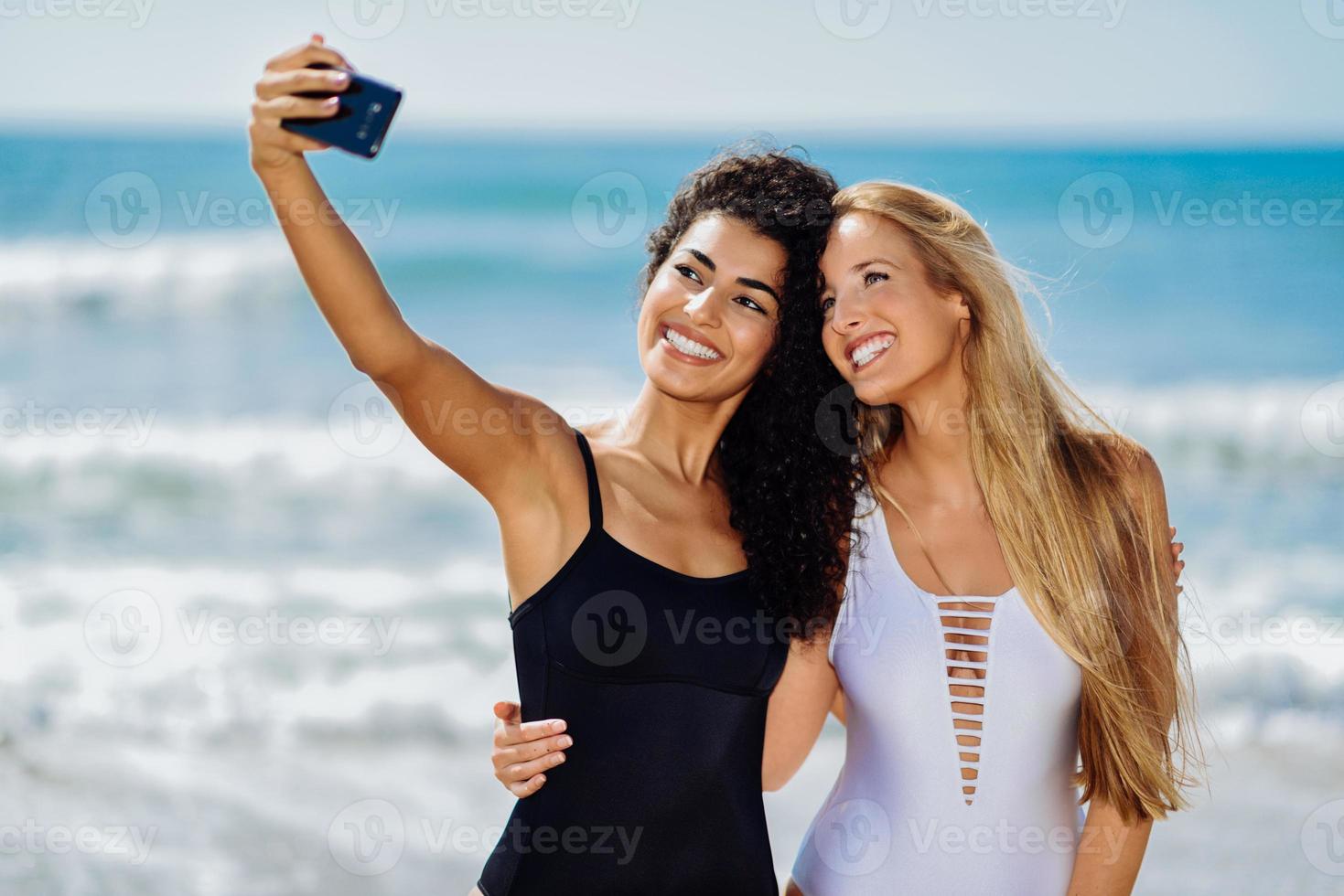 Dos mujeres tomando fotografías selfie con smartphone en la playa. foto