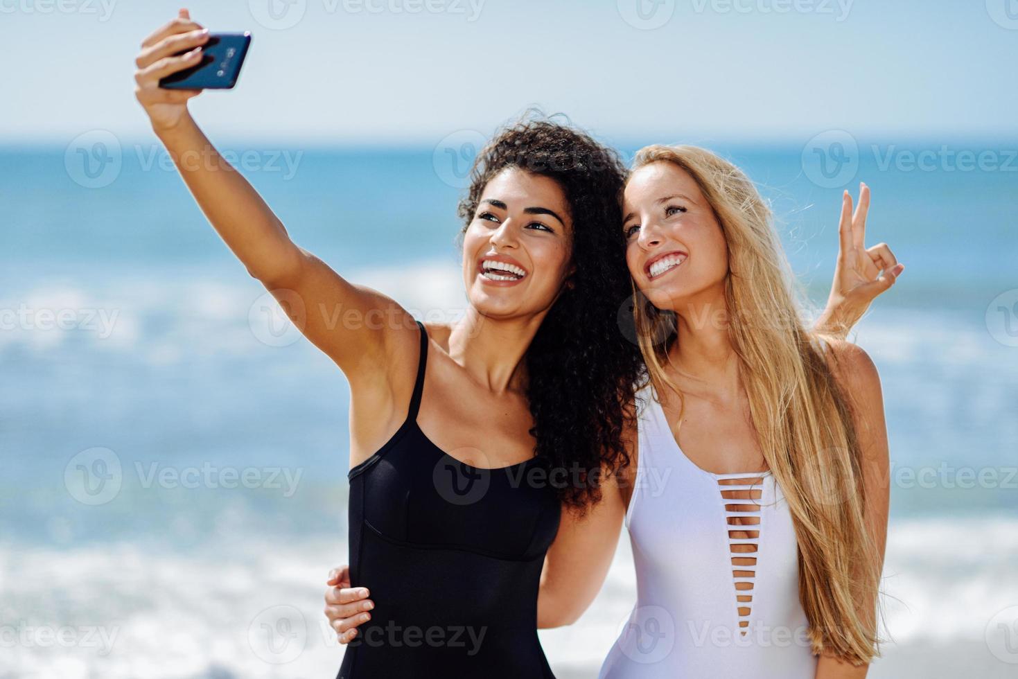 Two women taking selfie photograph with smartphone in the beach photo