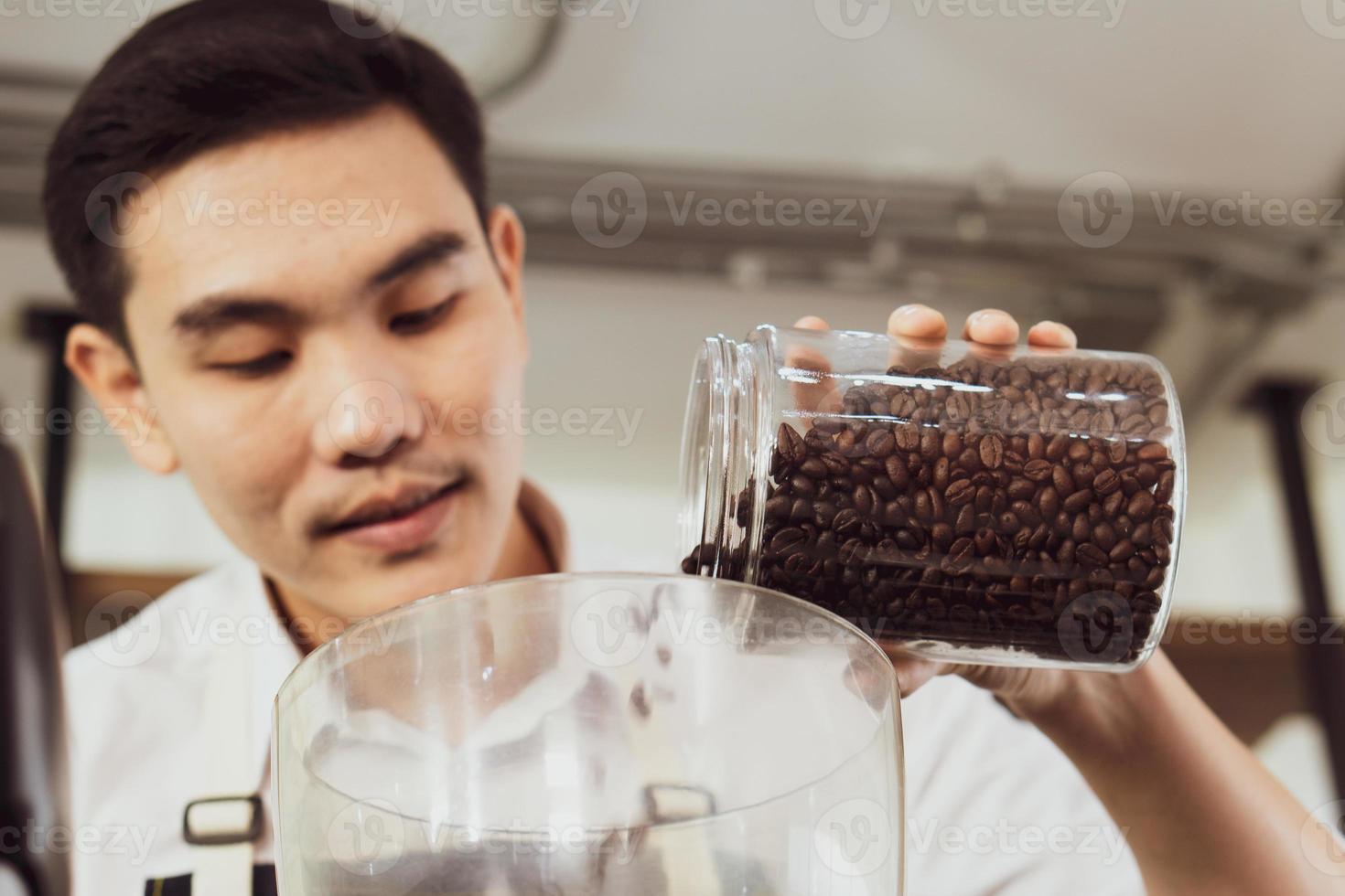 joven asiático llena los granos de café en la máquina trituradora. concepto de barista y cafetería foto
