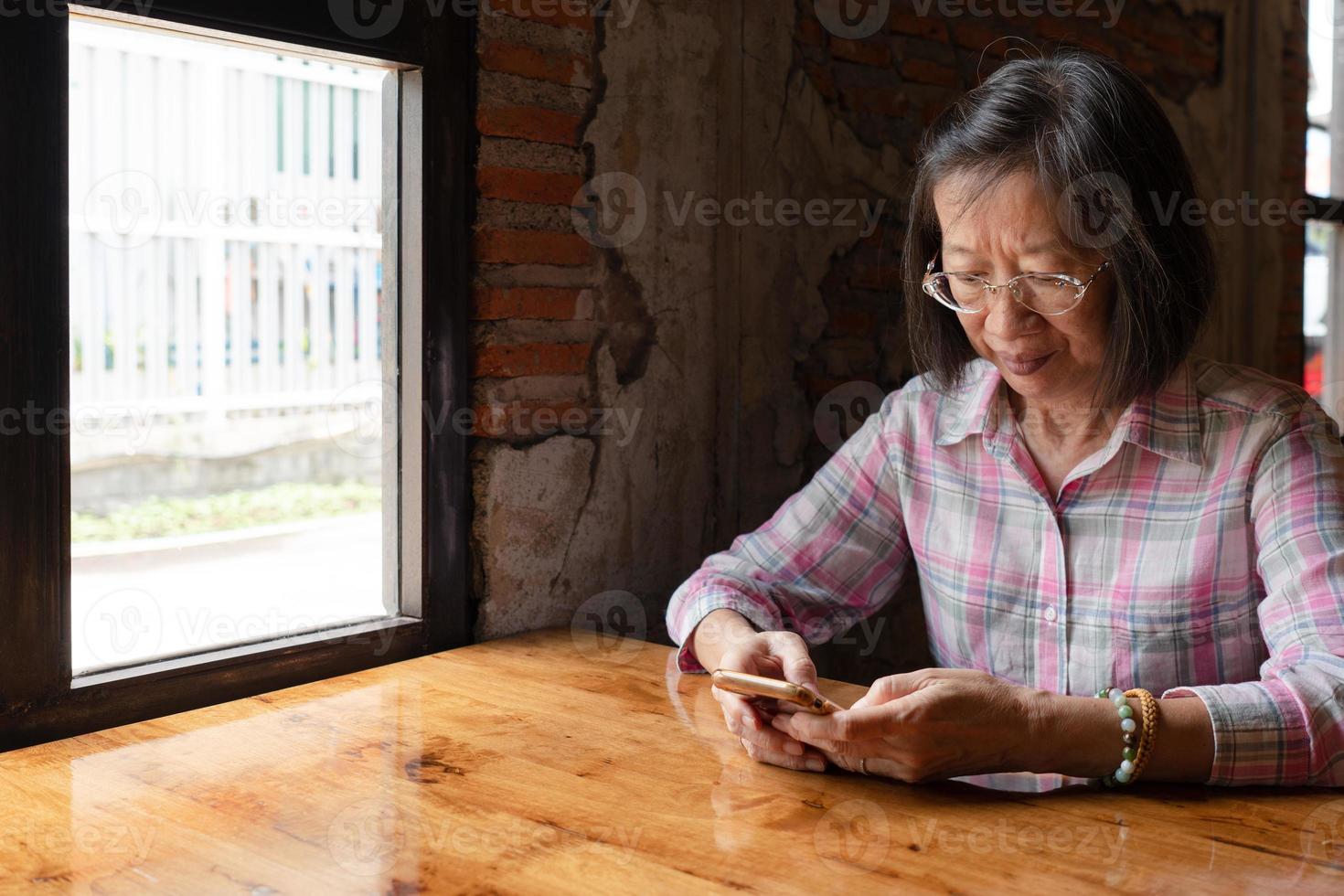 senior asian woman using smartphone while waiting in retro restaurant. happy retirement concept photo