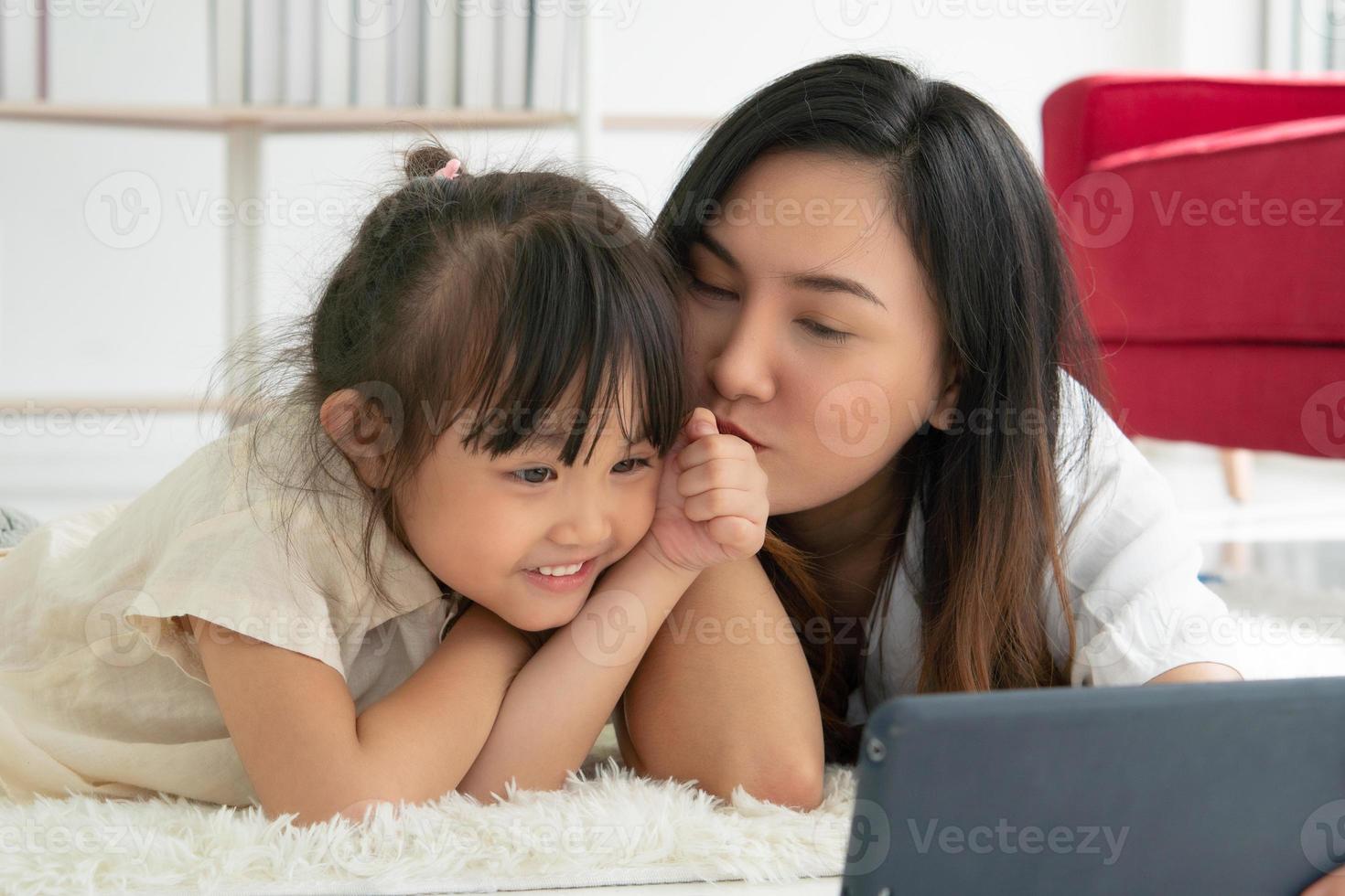 niño asiático besando a su madre mientras la madre usa la tableta para tomarles una foto en la sala de estar. concepto de familia unida