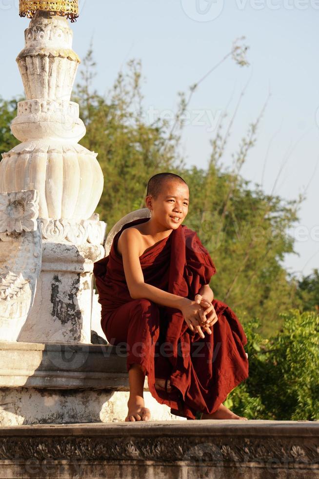 candid portrait of young asian smiling novice monk sitting at monasery photo