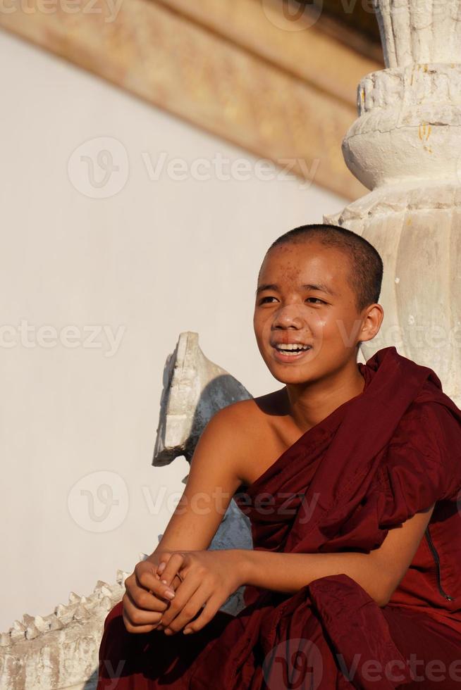 candid portrait of young asian smiling novice monk sitting at monasery photo