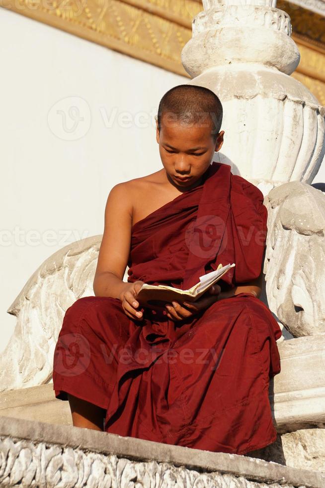 young asian novice monk reading book at monasery photo