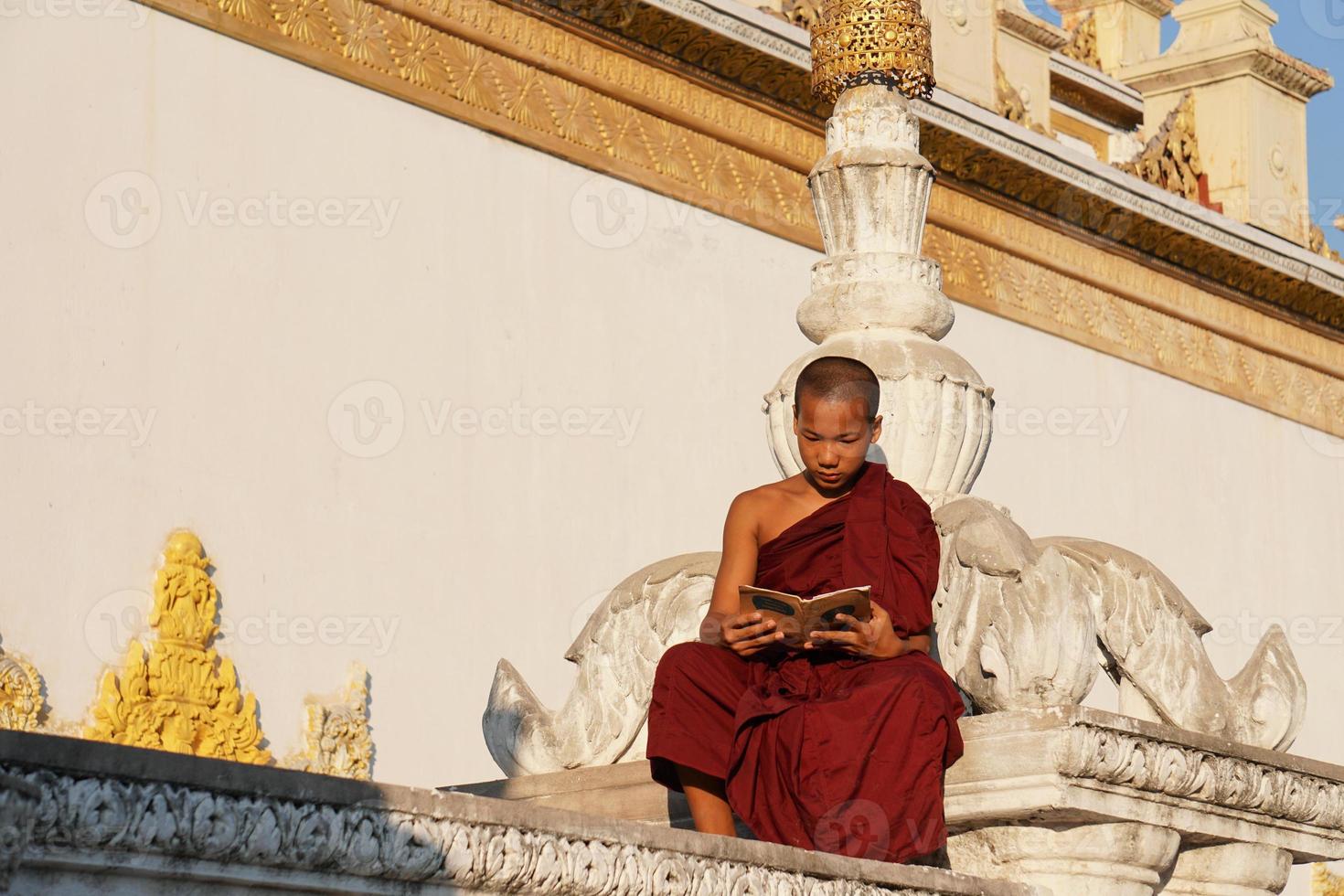 young asian novice monk reading book at monasery photo