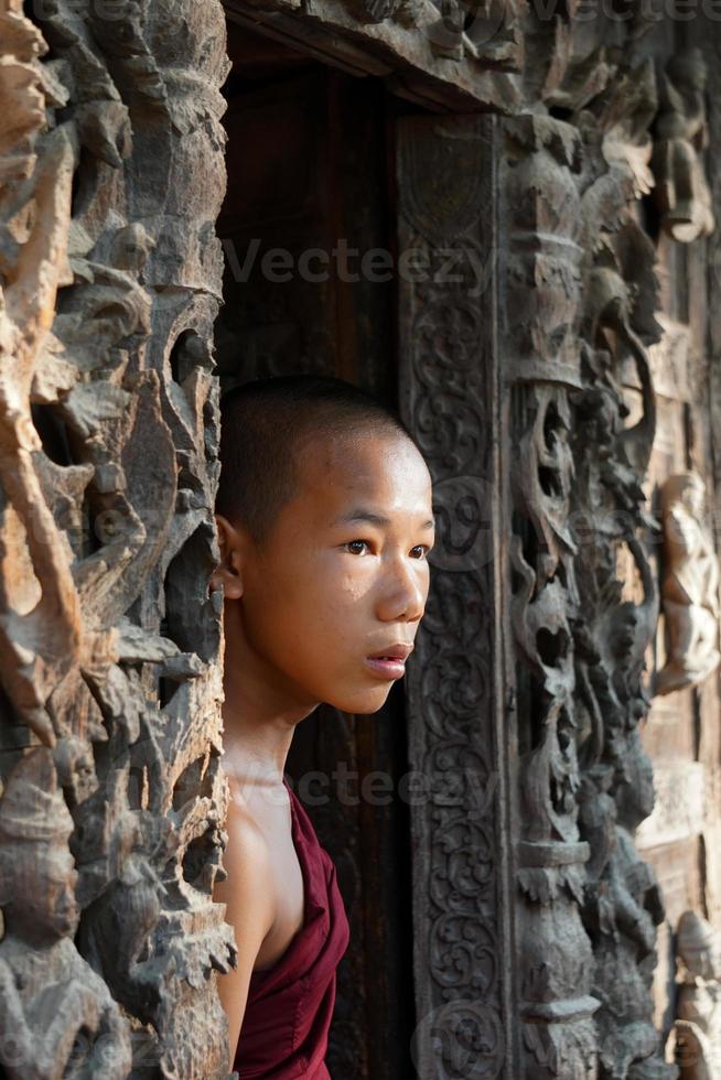 candid portrait of young novice monk standing at door of monasery photo