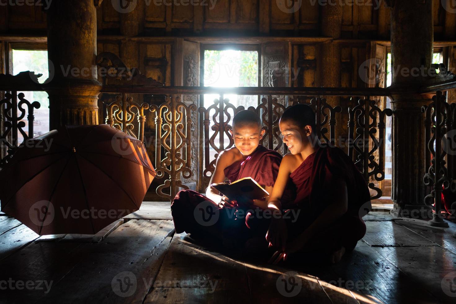 Dos jóvenes monjes novicios asiáticos leyendo un libro en el monasterio juntos foto