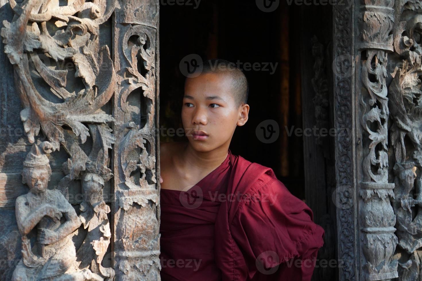 candid portrait of young novice monk standing at door of monasery photo