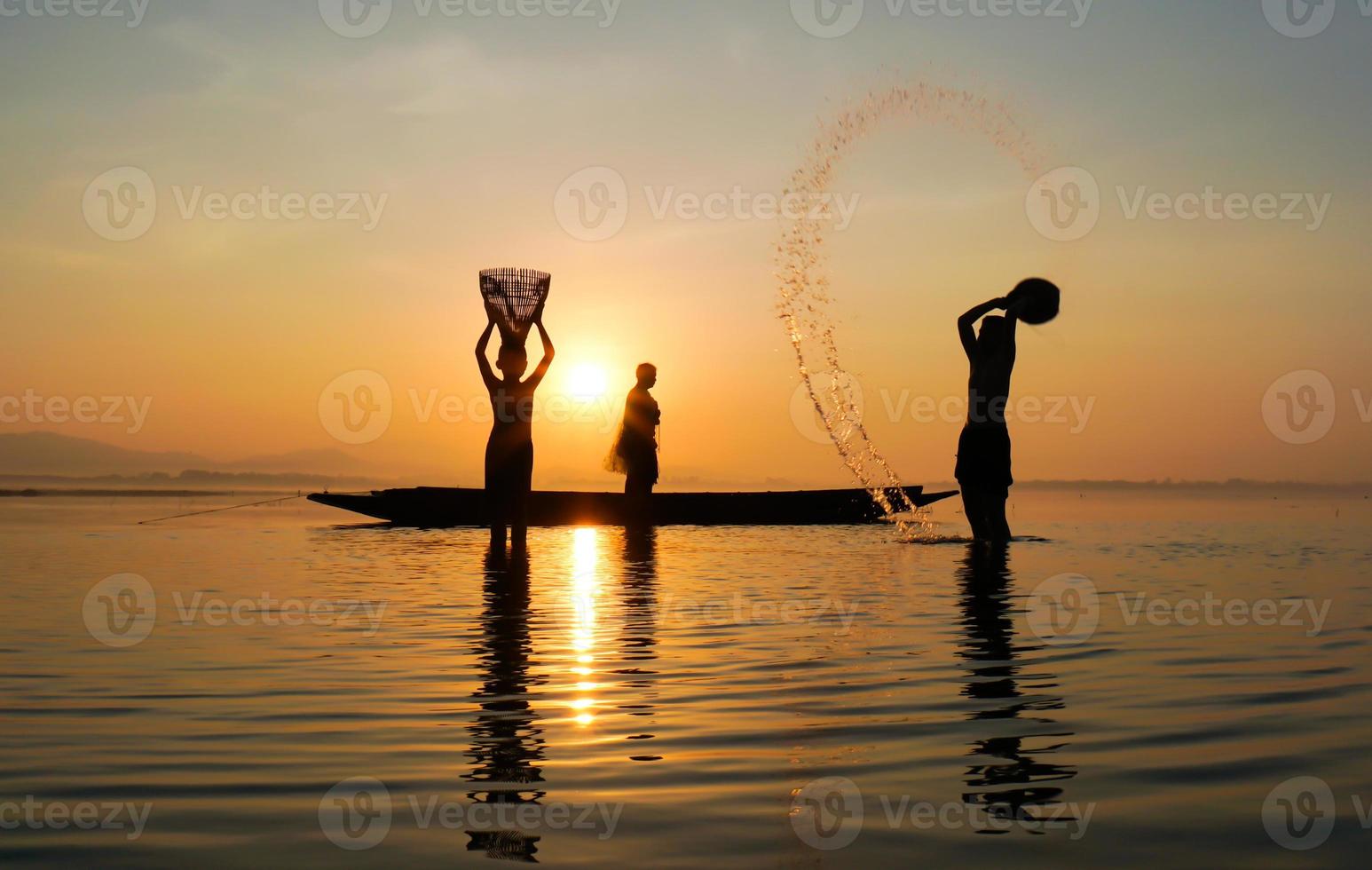 silueta de pescador y su hijo de pie en el lago cerca del barco y usando jar para salpicar agua foto