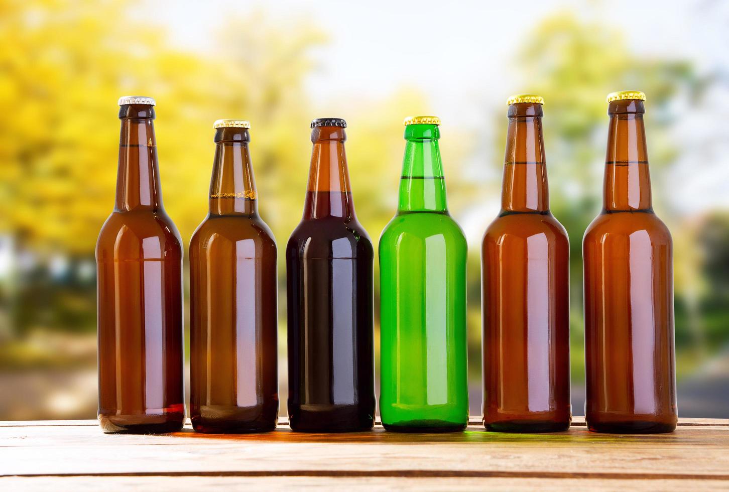 Botellas de cerveza de colores en la mesa sobre fondo borroso forrest, concepto de vacaciones foto