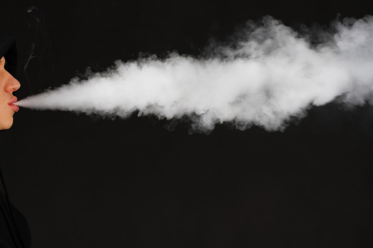 vaping hombre blanco sosteniendo un mod. una nube de vapor. fondo negro. vapear un cigarrillo electrónico con mucho humo. concepto de vape copia espacio enfoque selectivo foto