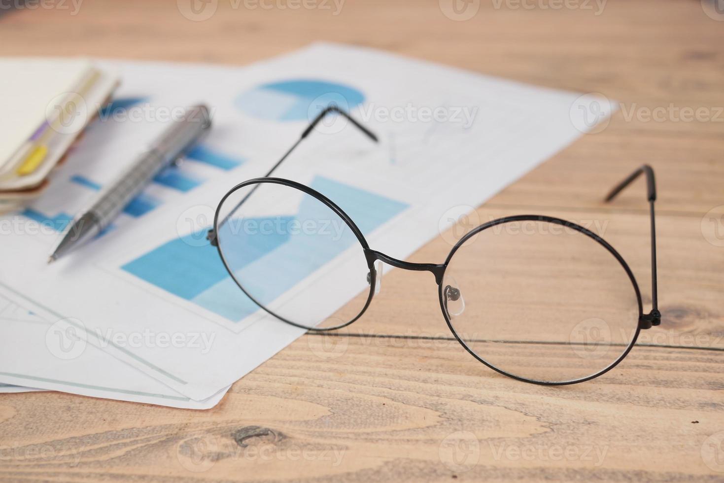 eyeglass, financial graph, calculator and notepad on table photo