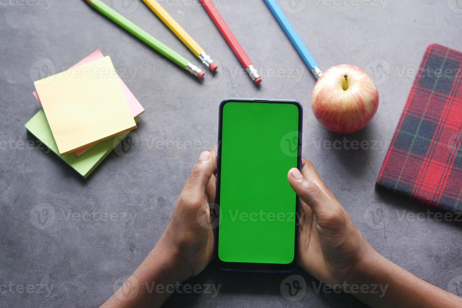 child hand holding smart phone with green screen on table photo