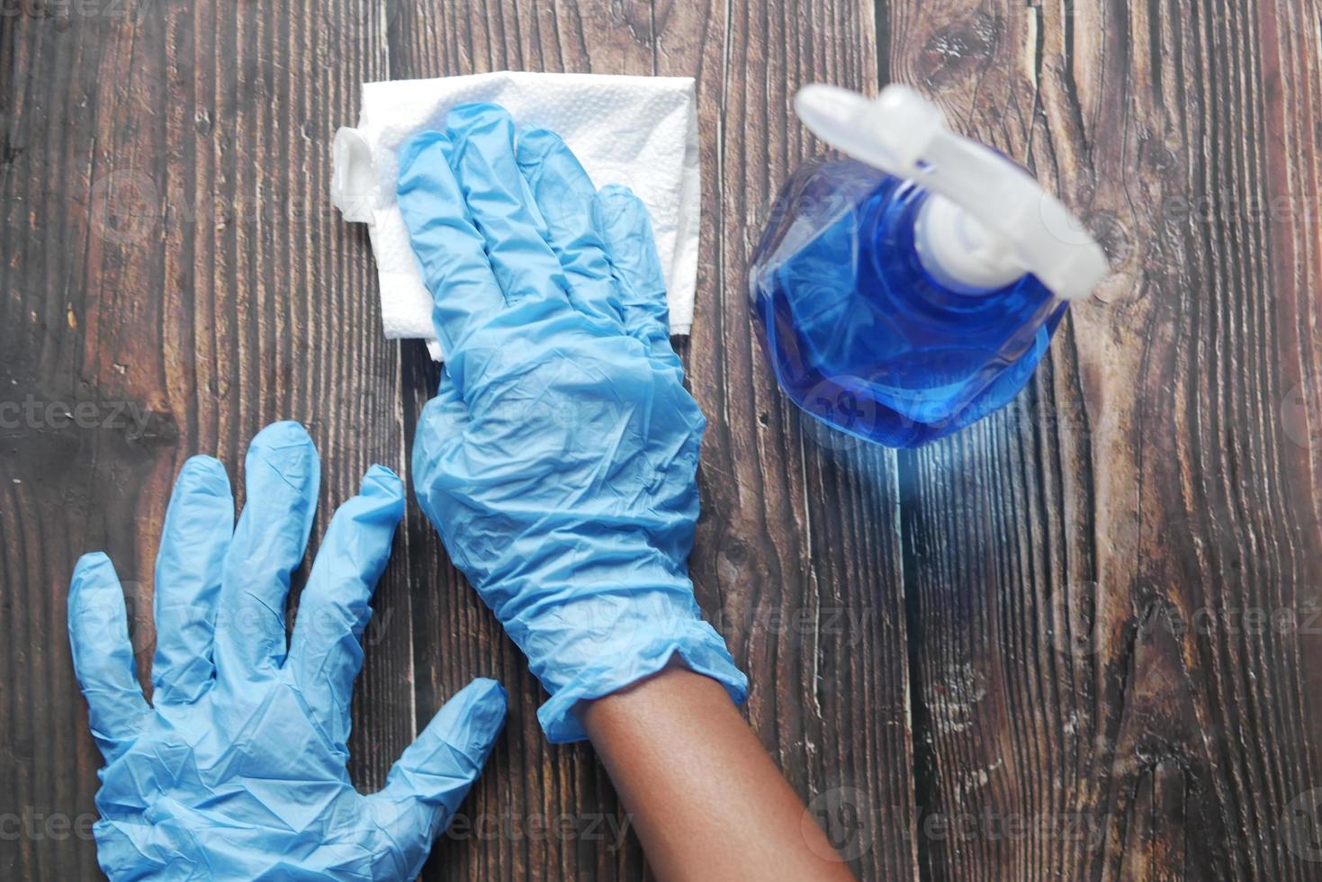 Mano en guantes de goma azul sosteniendo la mesa de limpieza de botellas de spray foto