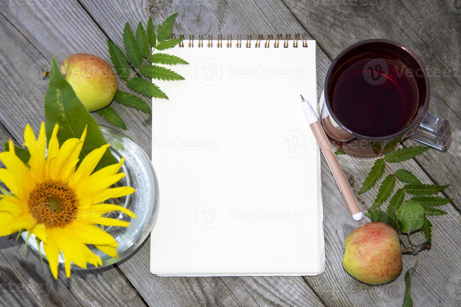 Bloc de notas con una hoja de papel en blanco para escribir. plantilla con un campo de texto. Fondo natural de bayas, flores y una bebida. serbal, girasol y manzanas. foto