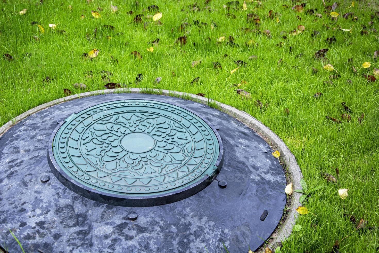 Sewer hatch. Yellow leaves on a green lawn. photo