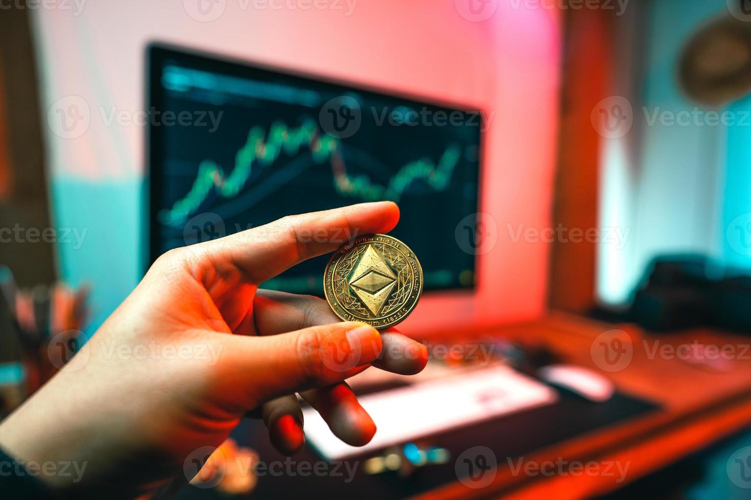 La mano de un hombre sostiene una moneda de eterio en una mesa de computadora. foto