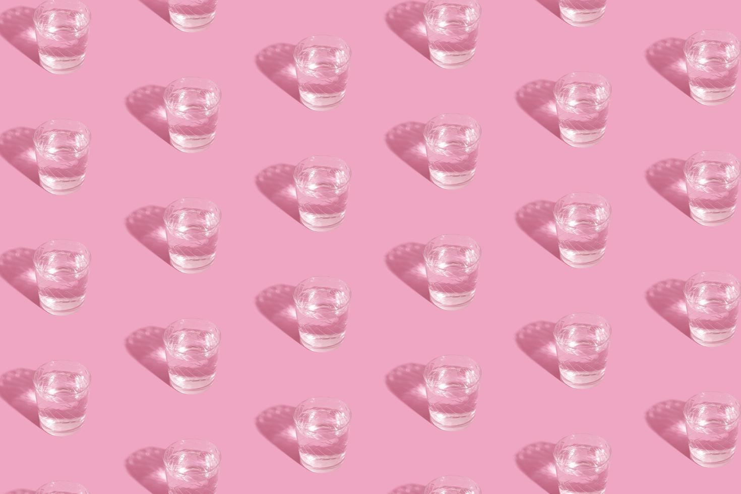 Glasses with water and shadow pattern on pink background photo