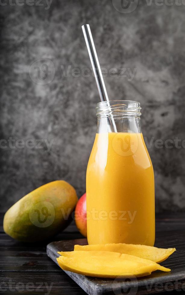 fresh mango shake in a glass with a metal drinking straw decorated with slices of mango front view on dark background photo