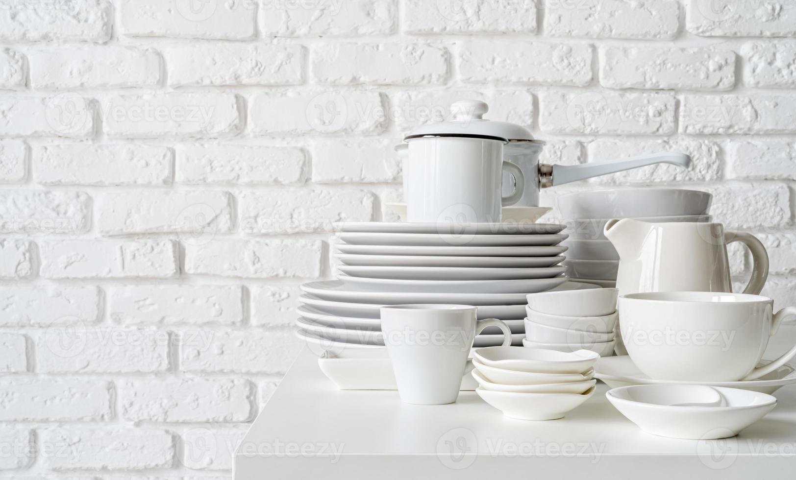 Pila de platos de cerámica blanca y vajilla sobre la mesa sobre fondo de pared de ladrillo blanco foto