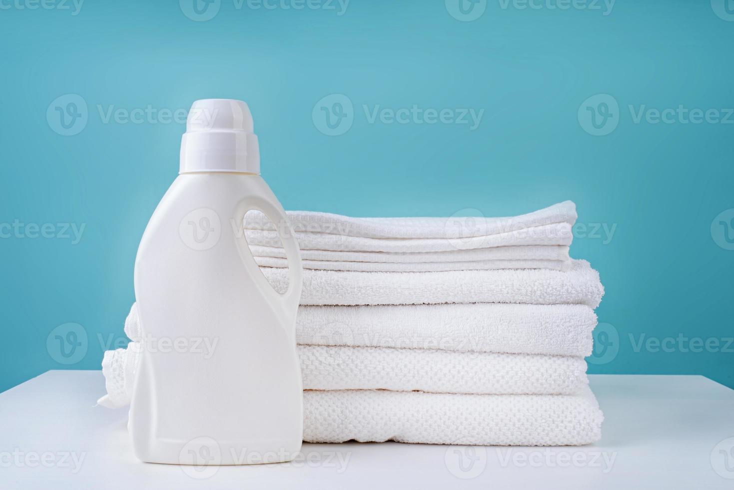 stack of clean white towels and a bottle of detergent on blue background photo