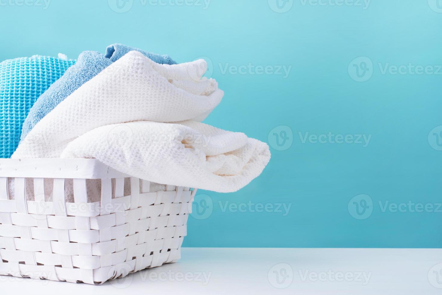 Pila de toallas limpias en una canasta de lavandería blanca sobre fondo azul. foto