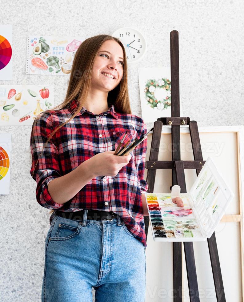 Hermosa mujer artista en camisa a cuadros pintando un cuadro en casa foto