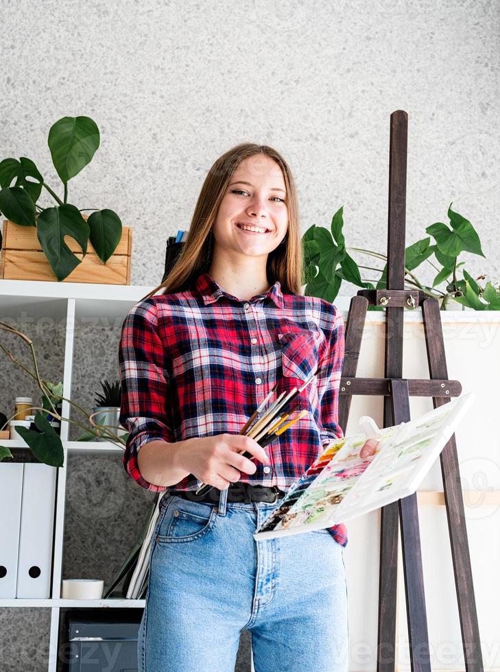 Hermosa mujer artista en camisa a cuadros pintando un cuadro en casa foto