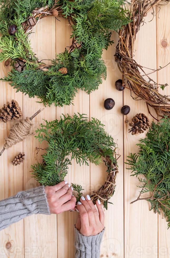 woman hands making christmas wreath craft on wooden background top view photo