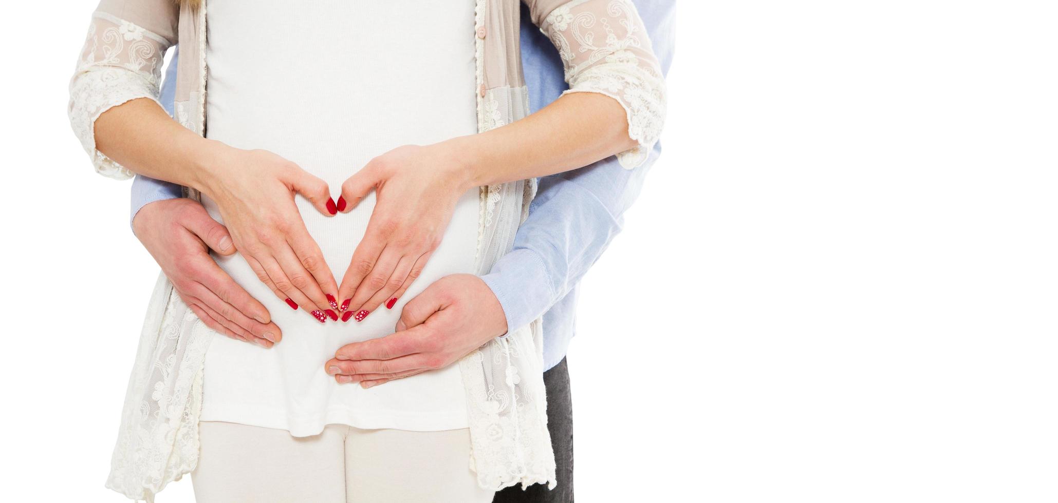 Retrato de una joven pareja embarazada sobre un fondo blanco muestran el signo de amor foto