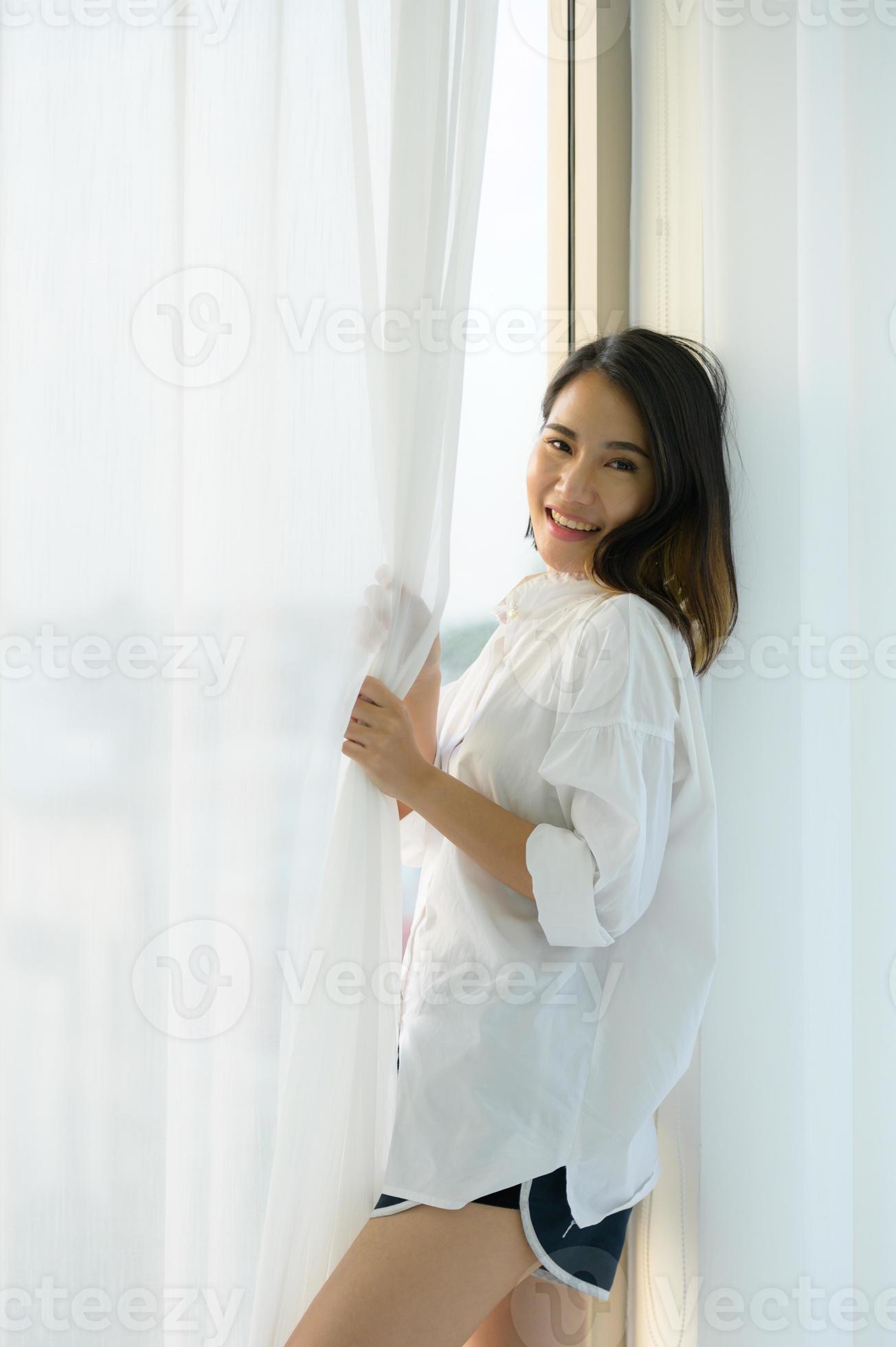 joven asiática en el dormitorio con cortinas blancas y el ambiente de la mañana cuando brilla el sol. foto
