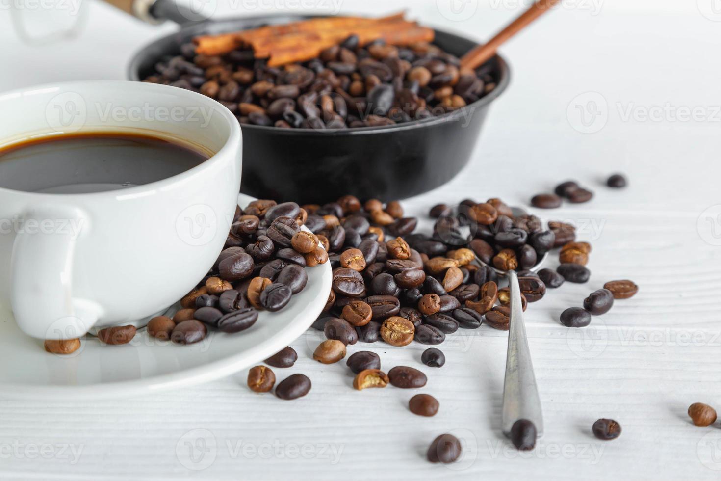 Taza de café y granos de café en la mesa de madera blanca foto