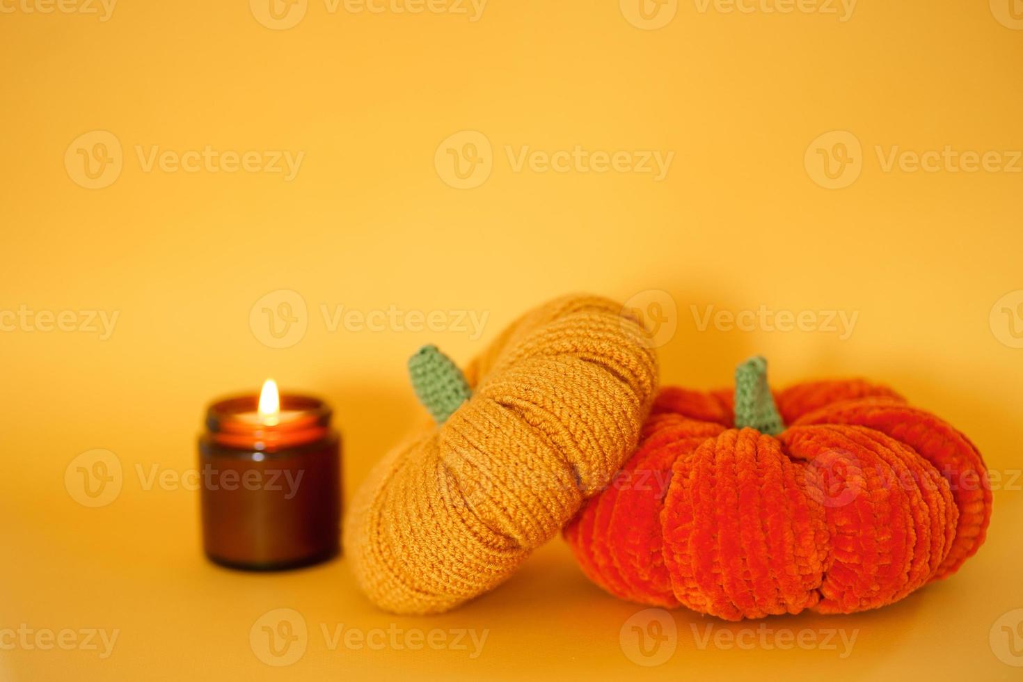 dos calabazas tejidas y una vela de soja encendida en un frasco de vidrio oscuro sobre un fondo amarillo. preparándose para halloween. relájate y cálmate. foto