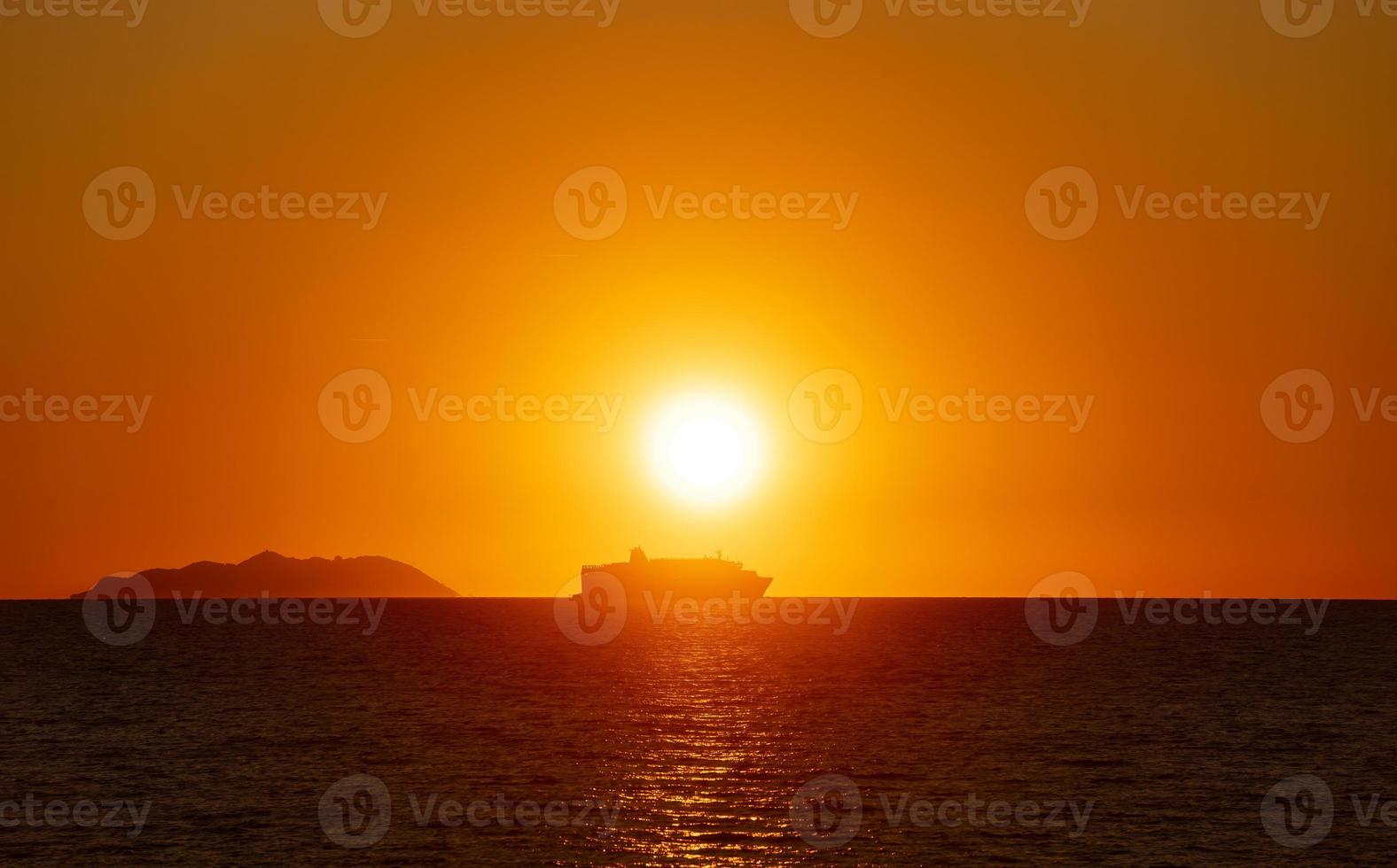 Un barco de pasajeros retroiluminado cerca de una isla al atardecer. foto