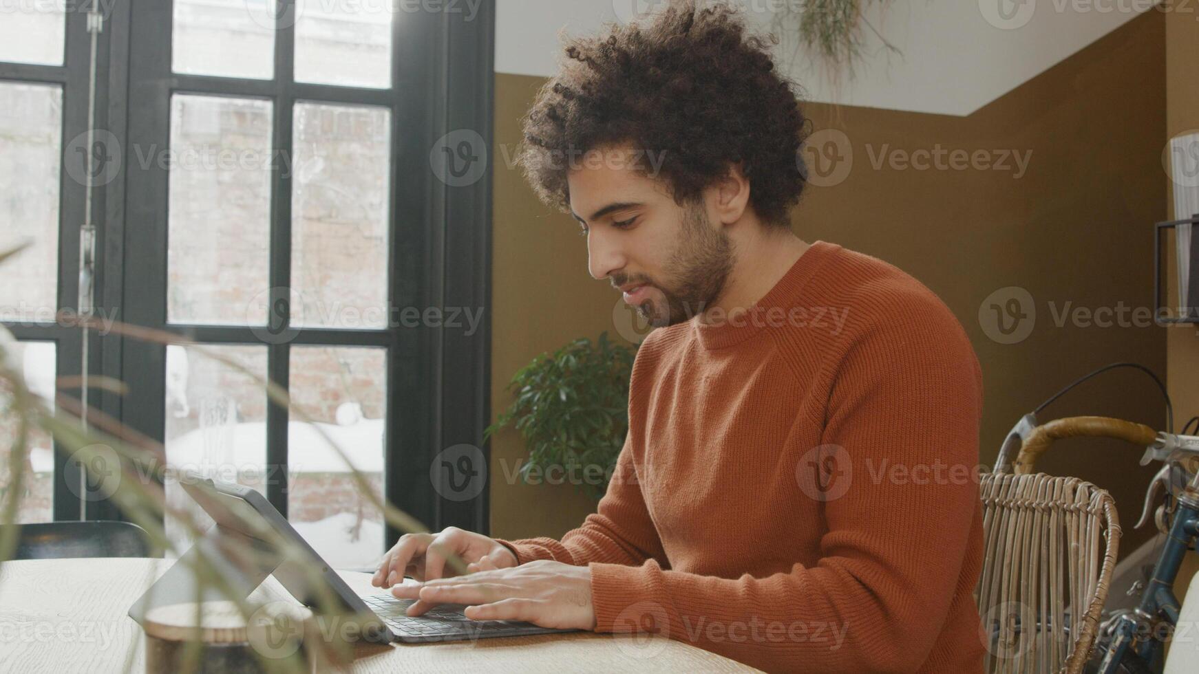 Young Middle Eastern man sits at table, typing on laptop, smiling and talking photo