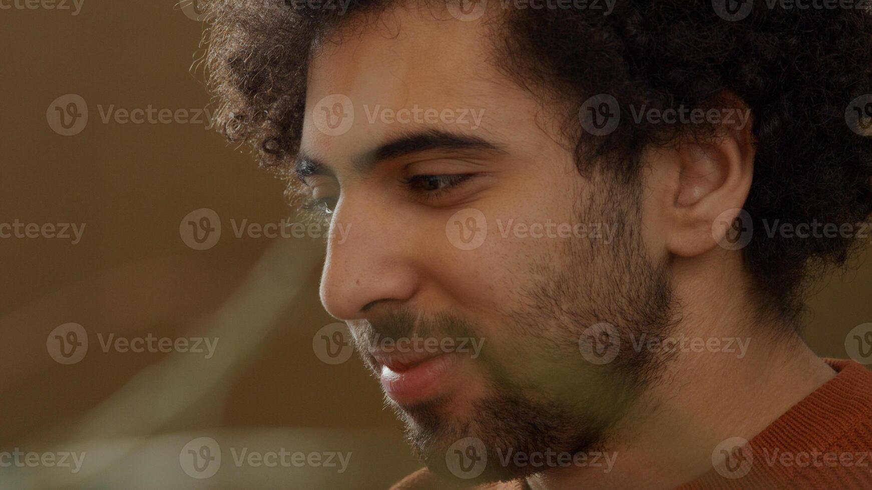 Close up of young Middle Eastern man, looks on laptop, smiles and talks photo