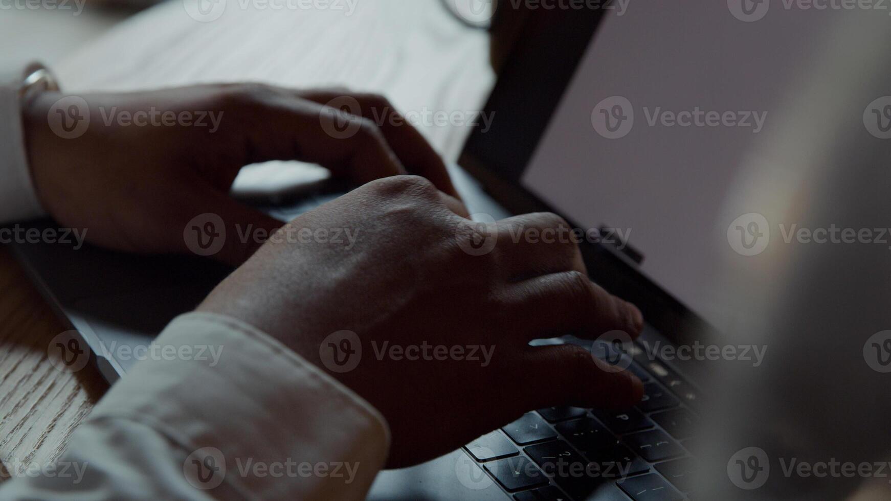 Black man wearing glasses, sitting at table, typing on laptop photo