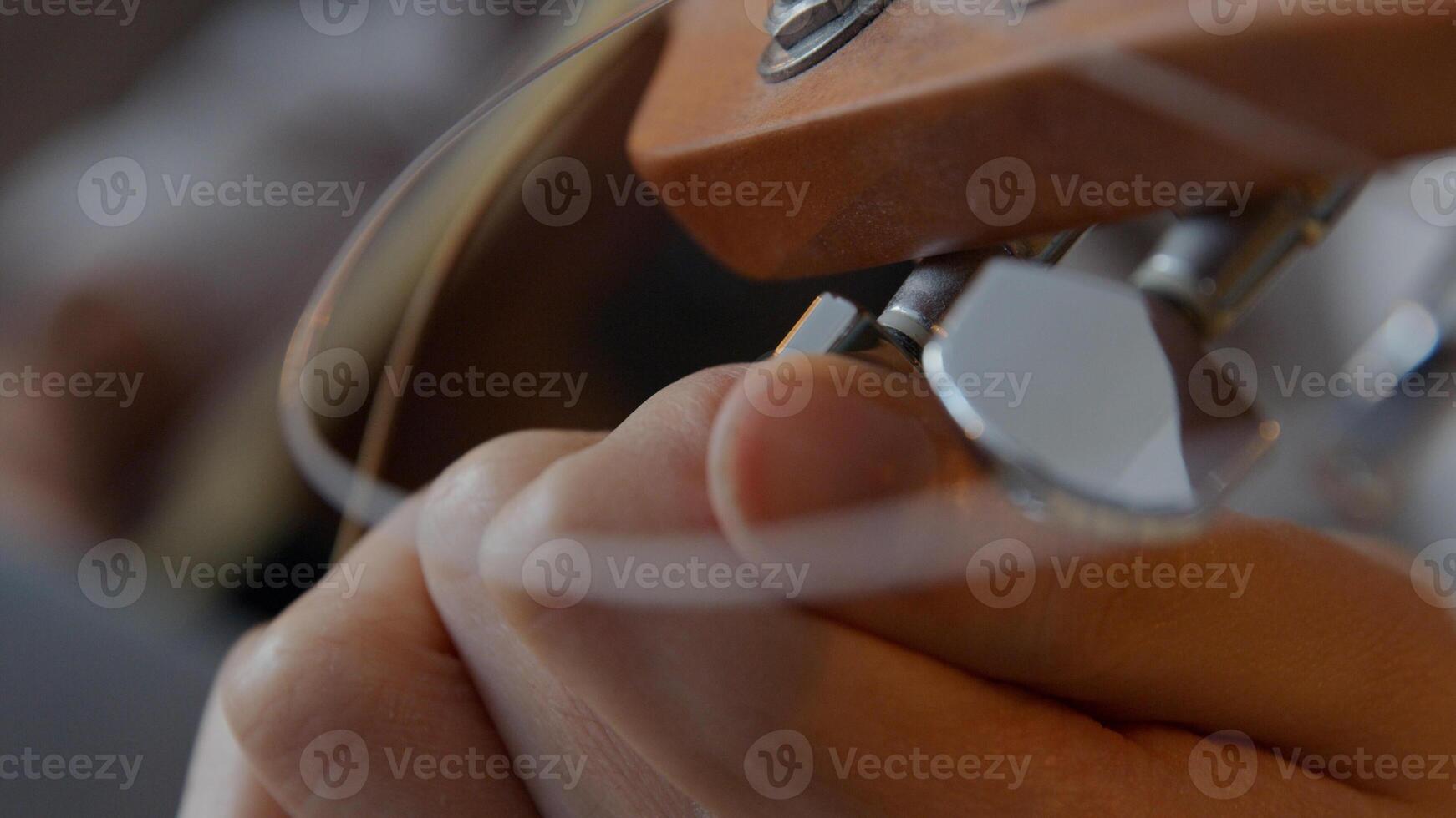 Cerca de los dedos de la joven mujer de raza mixta, girando el afinador de la guitarra, la otra mano toca la cuerda para afinar foto