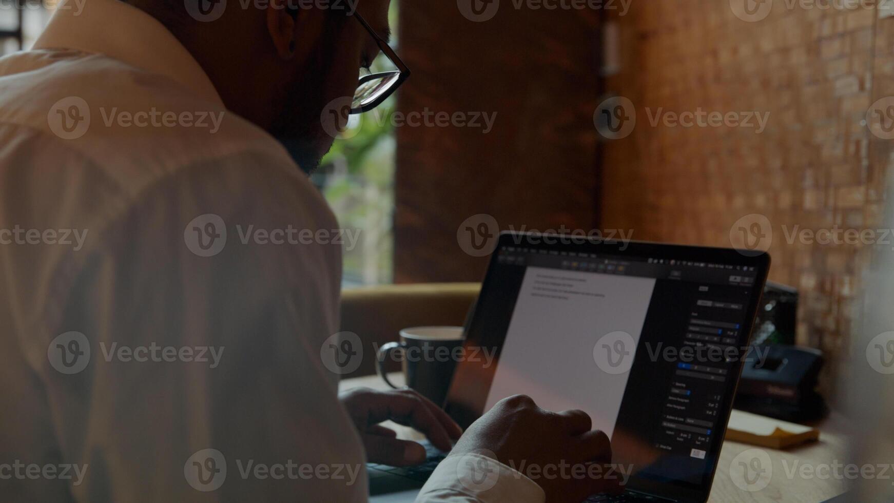 Black man wearing glasses, sitting at table, typing on laptop photo