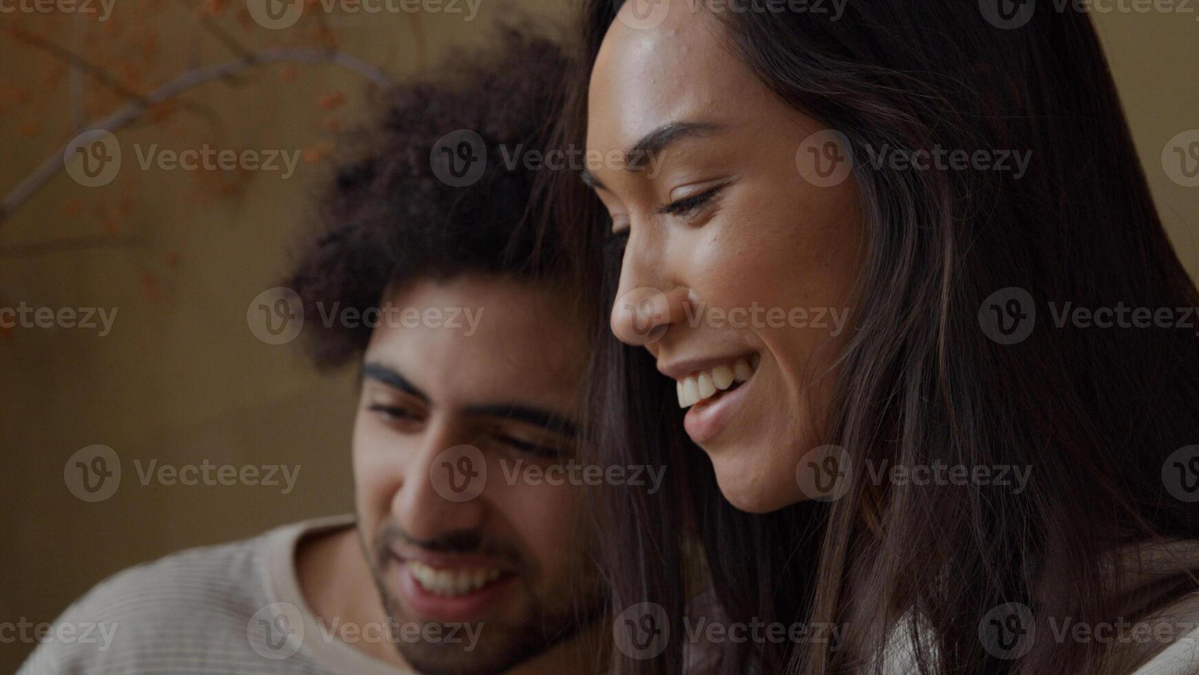 Young mixed race woman and young Middle Eastern man sitting on couch, woman holds phone, smiling, talking, both waving to phone photo